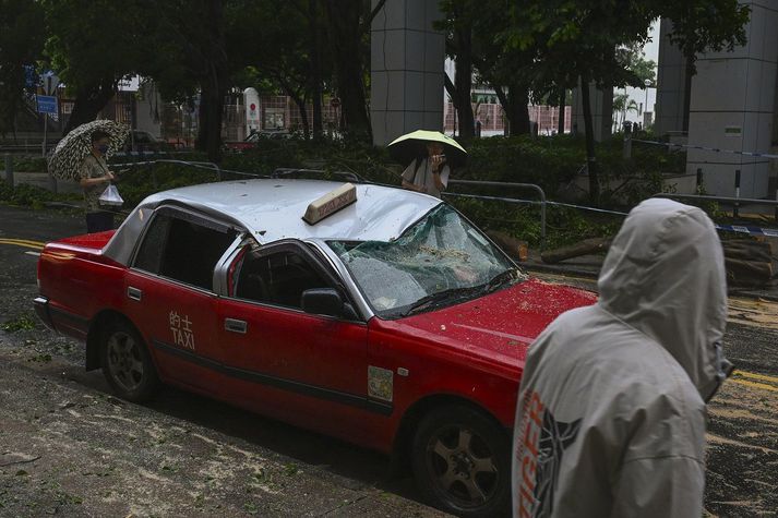 Íbúar virða skemmdan leigubíl fyrir sér í Hong Kong.