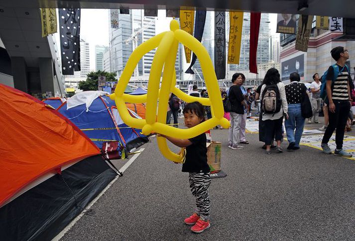 Stúlkubarn með uppblásna gula regnhlíf á svæði því sem mótmælendur hafa lagt undir sig fyrir utan stjórnarbyggingarnar í Hong Kong í gær. Regnhlífar eru tákn mótmælanna og hafa verið sett upp á svæðinu nokkur listaverk með regnhlífarþema.