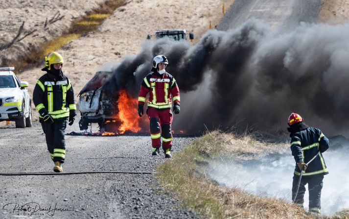 Slökkviliðsmenn á Svínvetningabraut á sunnudaginn. Tvinnbíllinn í ljósum logum í bakgrunni.