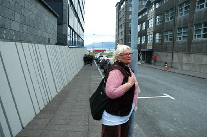 Aðalheiður Gunnlaugsdóttir stendur fyrir framan bankann. Hópur af lögreglumönnum sést fyrir aftan hana en þeir vönduðu henni ekki kveðjurnar.