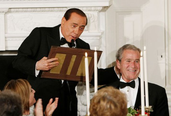 Silvio Berlusconi heldur á hluta púltsins við mikla kátínu George Bush.