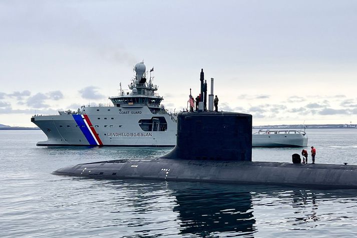 Tveir áhafnarmeðlimir baksa ofan á USS Delaware. Landhelgisgæslan fylgist vel með í bakgrunni.