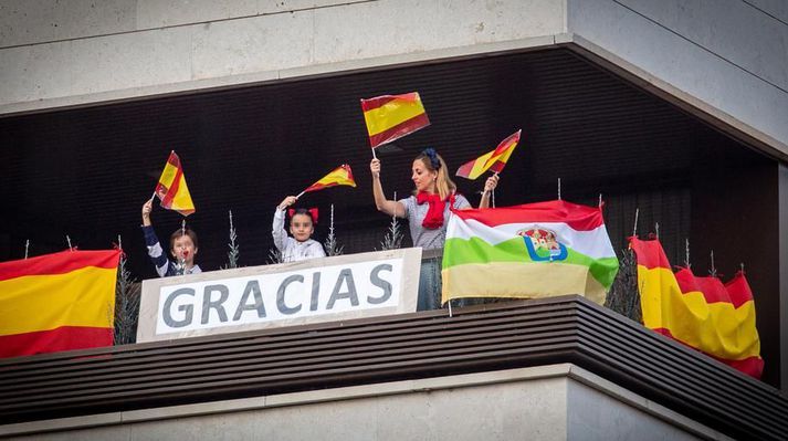 Kona og börn veifa spænskum fánum og klappa til að heiðra heilbrigðisstarfsmenn og lögreglu í kórónuveirufaraldrinum í borginni Logroño í La Rioja-héraði. Börn hafa þurft að vera alfarið innandyra í útgöngubanninu.