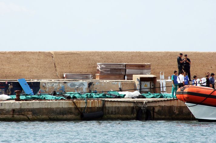 Tugir flóttamanna eru taldir af eftir að eldur kom upp í skipi út af ítölsku eyjunni Lampedusa í morgun. Hér sjást björgunarmenn við lík flóttafólksins á höfninni í Lampedusa.