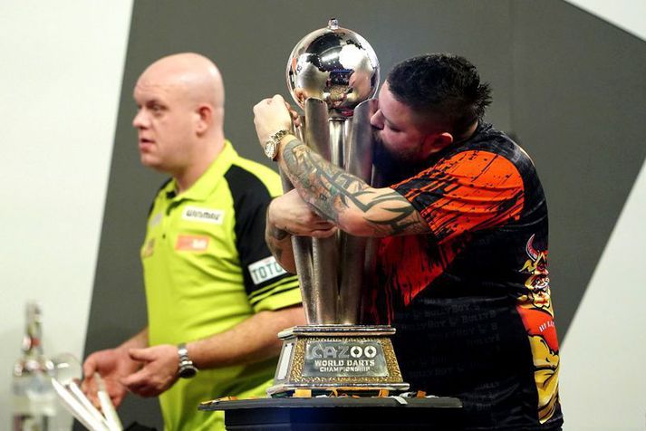 Michael Smith kyssir heimsbikarinn eftir sigur sinn Michael van Gerwen sem sést í bakgrunni.