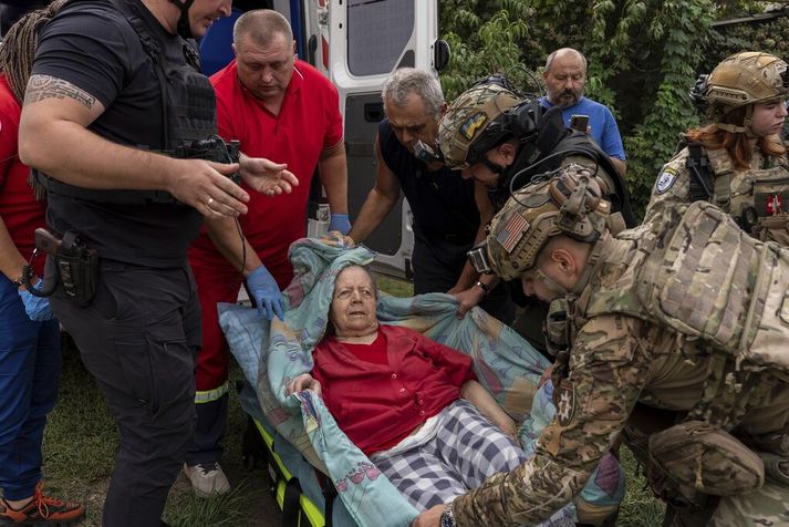Lögreglumenn og sjúkraliðar bera konu á níræðisaldri sem særðist þegar rússnesk svifsprengja lenti á þorpinu Jarova í Donetsk í dag.
