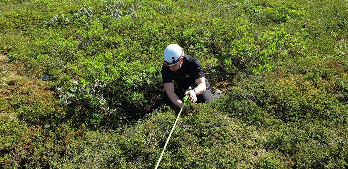 Björgunarsveitarmaður sígur niður í sprunguna til að koma ólum á hvutta.