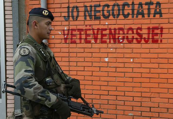 KFOR-hermaður í Kos-ovska Mitrovica. Á vegginn er krotað á albönsku: „Enga samninga – sjálfstæði!“