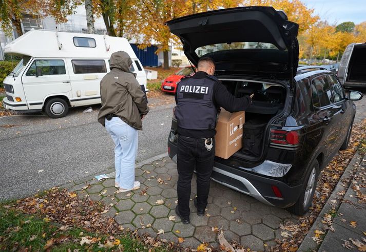 Lögreglumaður kemur kassa með munum sem hald var lagt á í húsleit hjá samtökum íslamista fyrir í skotti bíls í Hamborg í dag.