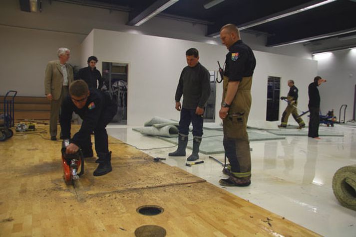 Slökkviliðsmenn rjúfa gólfið í íþróttasalnum.