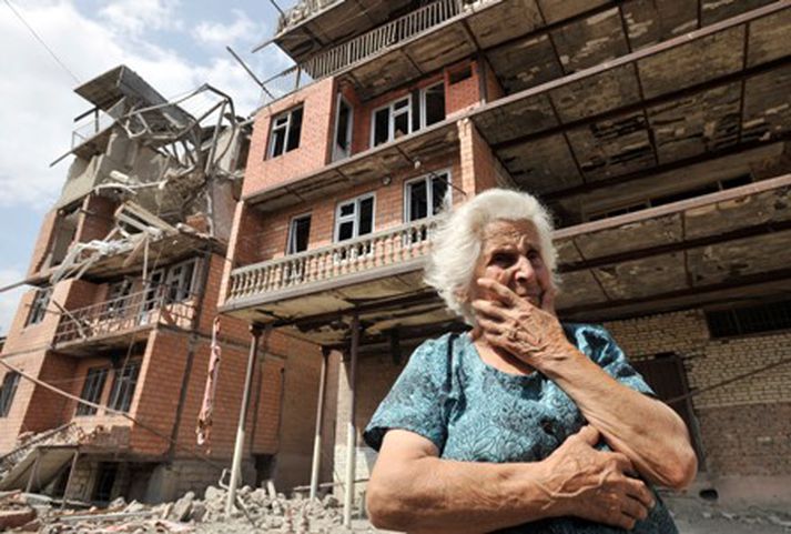 Georgísk kona við illa farið húsið sitt í Gori í Georgíu.