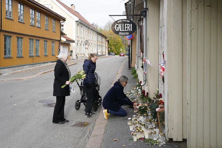 Þrjár konu leggja blóm og kerti til minningar um fórnarlömb árásarinnar í Kongsberg.