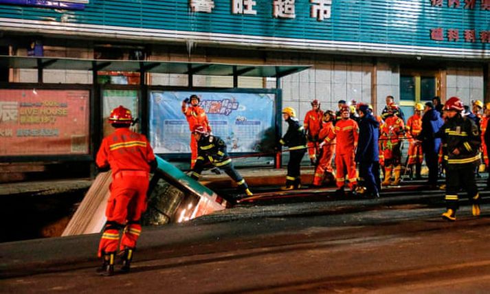 Farþegar og gangandi vegfarendur féllu ofan í holuna. Hér má sjá slökkviliðsmenn að störfum, sem að lokum tókst að lyfta rútunni úr holunni.