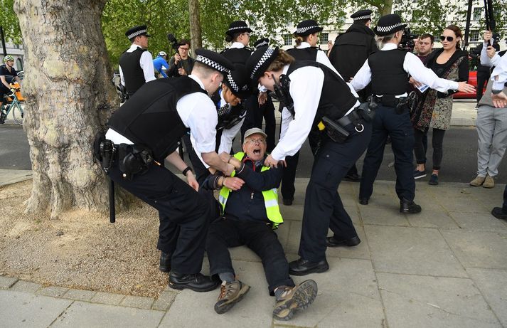 Lögregluþjónar handtaka mótmælanda sem er andvígur félagsforðun við mótmæli sem fóru fram í London í gær.