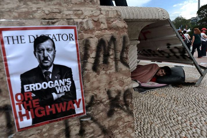 Maður fær sér lúr á Taksim-torgi í Istanbúl nærri veggspjaldi þar sem Recep Tayyip Erdogan, forsætisráðherra landsins, er sýndur í gervi Hitlers. Í landinu halda áfram mótmæli þar sem krafist er aukins frjálsræðis, en þeim hafa stjórnvöld mætt af mikilli hörku.