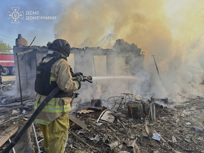 Slökkviliðsmaður dæli vatni á rústir íbúðarhúss eftir loftárás Rússa í Donetsk-héraði í Austur-Úkraínu í morgun.