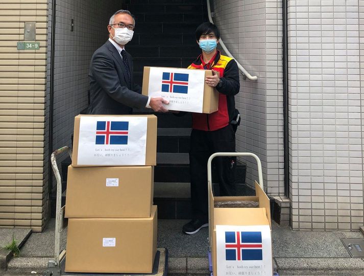 Hér sést forstjóri japanska sýnaglasa-framleiðandans afhenda DHL hraðsendingaþjónustu fyrstu sendinguna af sýnaglösum. Á sendingunni er íslenski fáninn og skilaboð um að nú gerum við okkar besta.