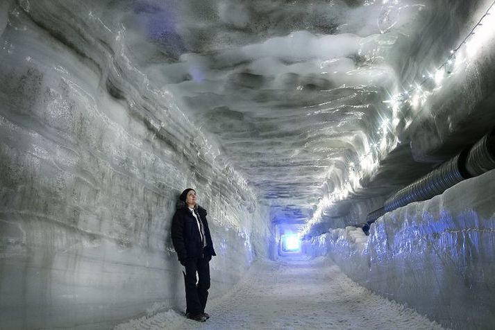 Þar til led-ljósum hefur verið komið fyrir í ísnum eru undirheimar jökulsins lýstir upp með jólaseríum. Loftræstirör í veggnum víkja og göngin breikka er vinnuvélarnar hafa unnið sitt verk. Fjær sést í gangamunnann.