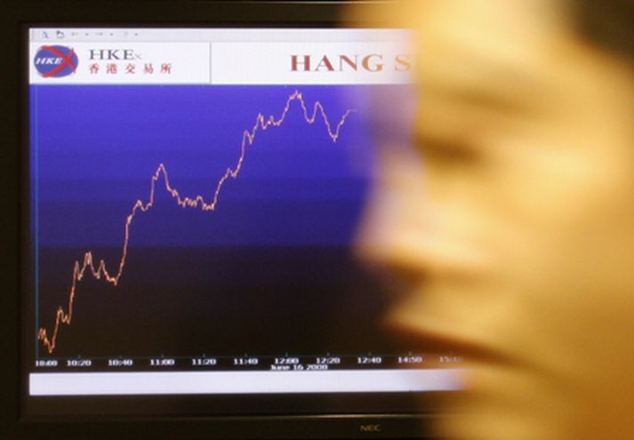 Maður gengur fram hjá skjá sem sýnir hreyfingar Hang Seng-vísitölunnar í Hong Kong.