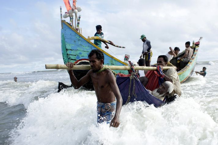 Tveir flóttamenn úr röðum Rohingja bera gamlan mann.