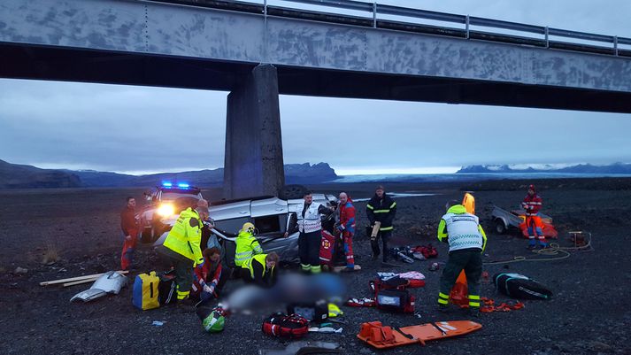 Toyota Land Cruiser-bíllinn á sandinum fyrir neðan brúna. Aðkoma björgunarfólks var hrikaleg eins og hér má sjá. Hluti myndarinnar hefur verið máður út.